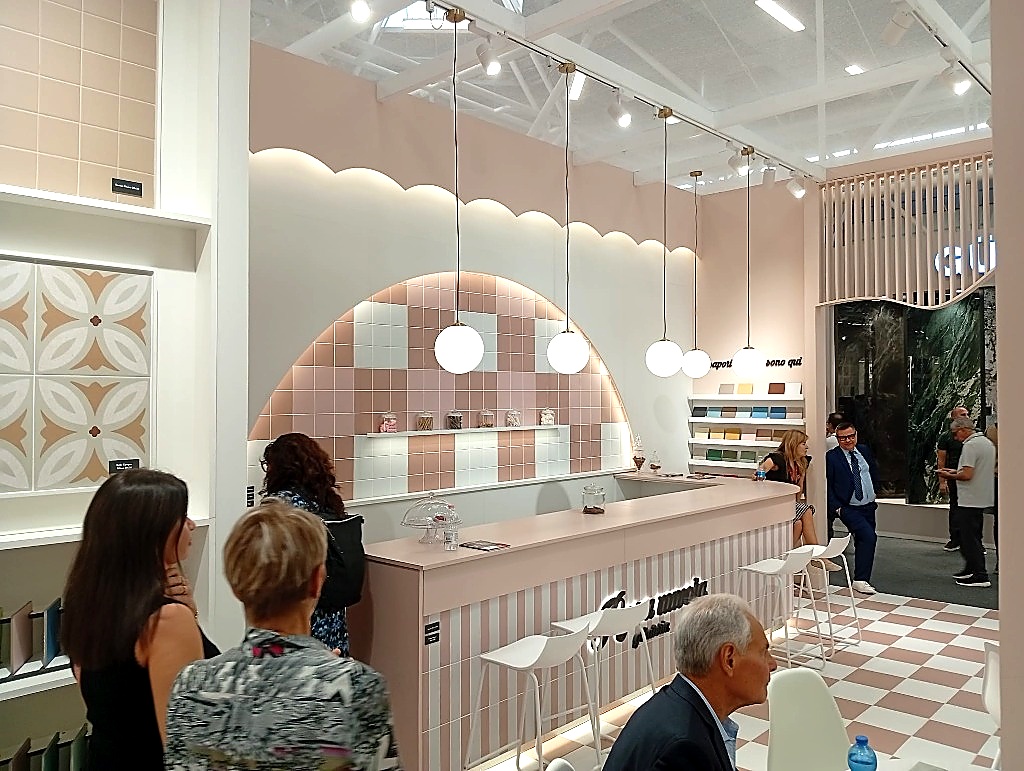 Stand espositivo allestito come una pasticceria confetteria con arco a nuvola rosa e bancone a righe bianche e rosa